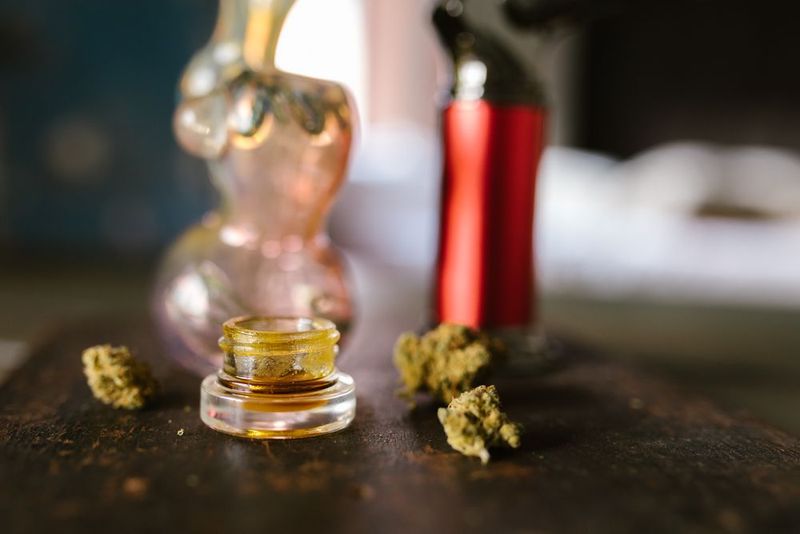 Jar of golden cannabis concentrate beside dried buds