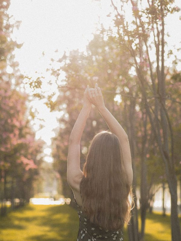 Woman seen from behind with arms raised in a sunlit park